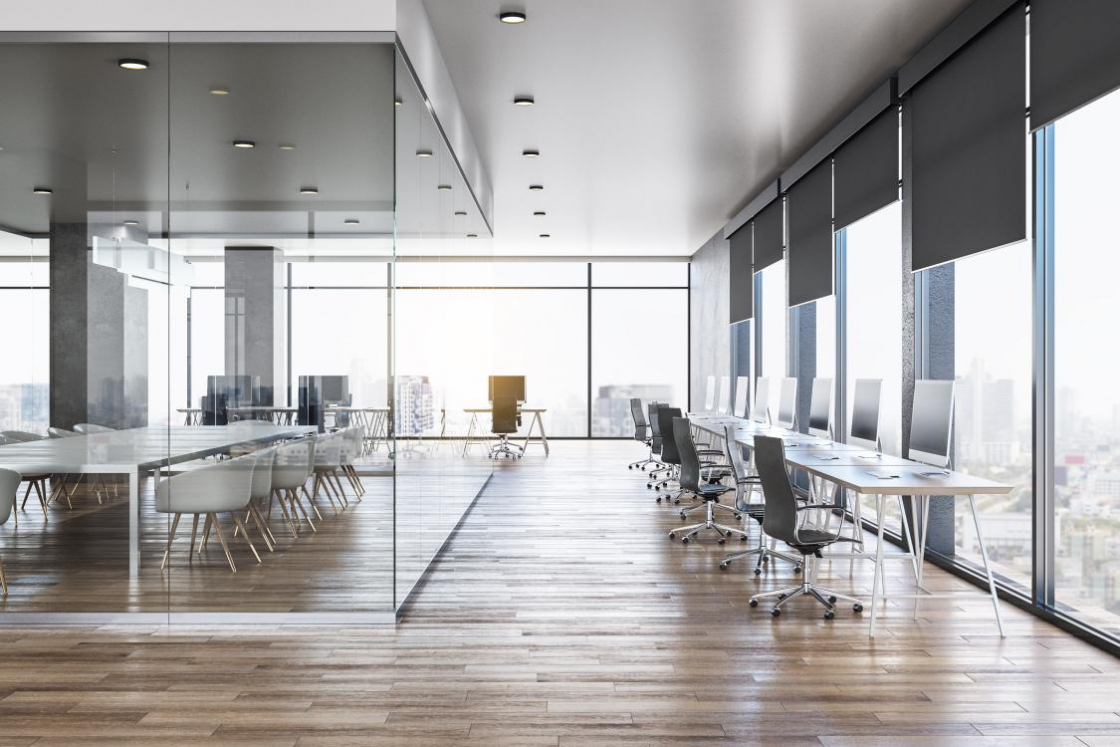 A row of desks and a meeting room in a large commercial office.