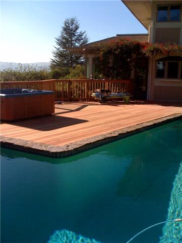 A backyard deck built up to a swimming pool with a jacuzzi on it.