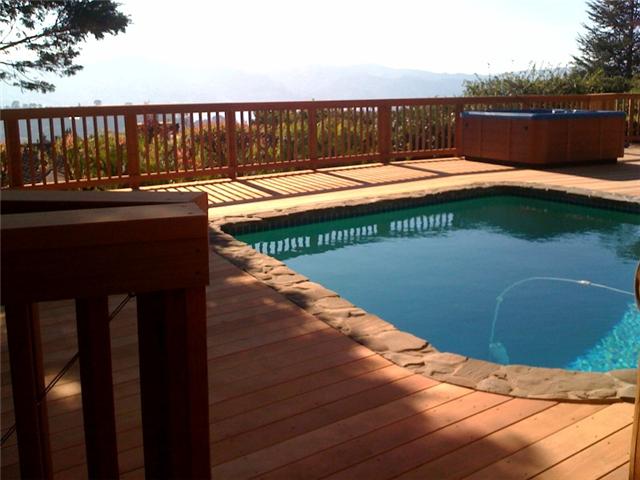 A deck in a residential houses backyard that leads up to and integrates with a pool.