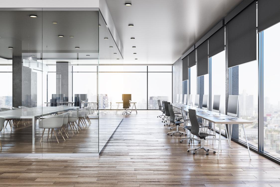 A row of desks and a meeting room in a large commercial office.