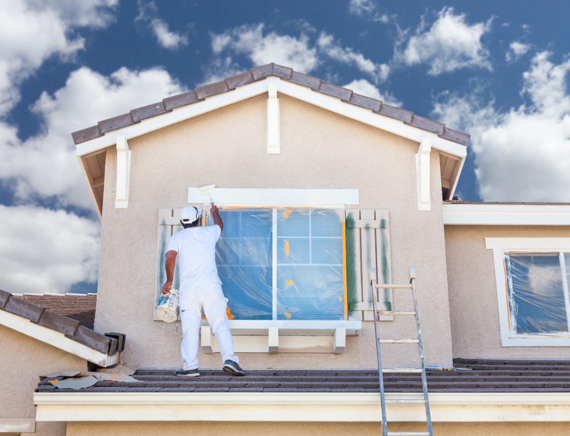 Man painting the outside trim of a window on a residential house.